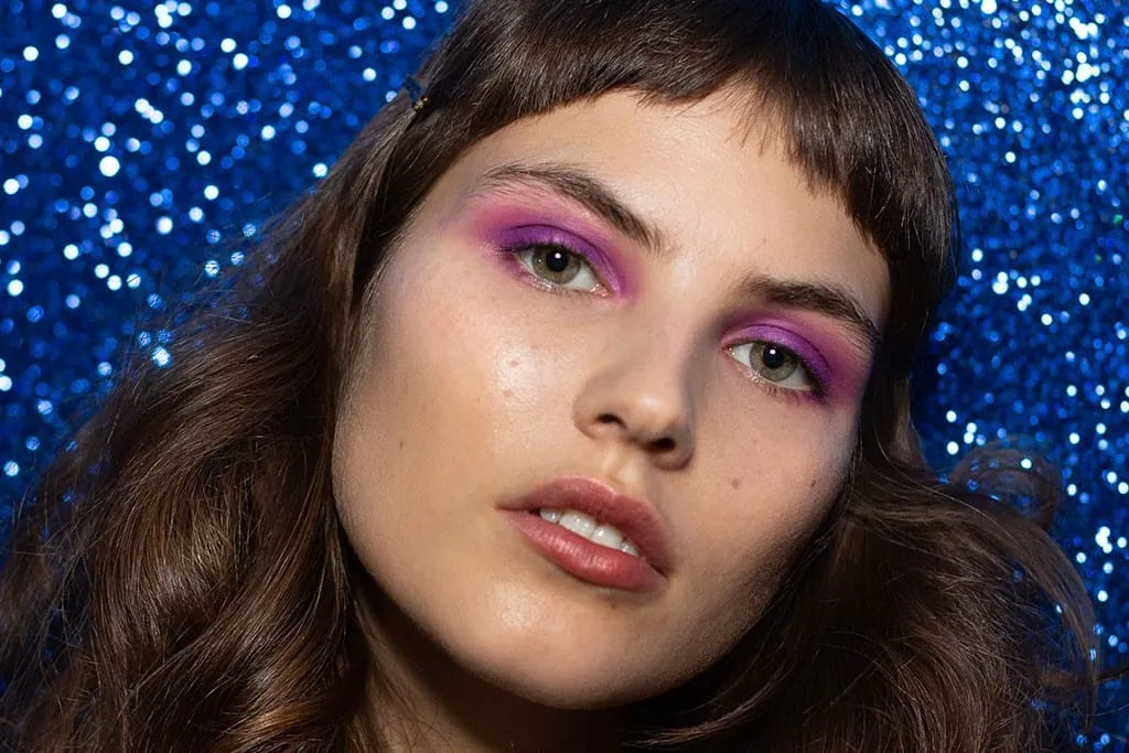 Bright pink and lilac disco eye make-up shot against a blue sequin backdrop