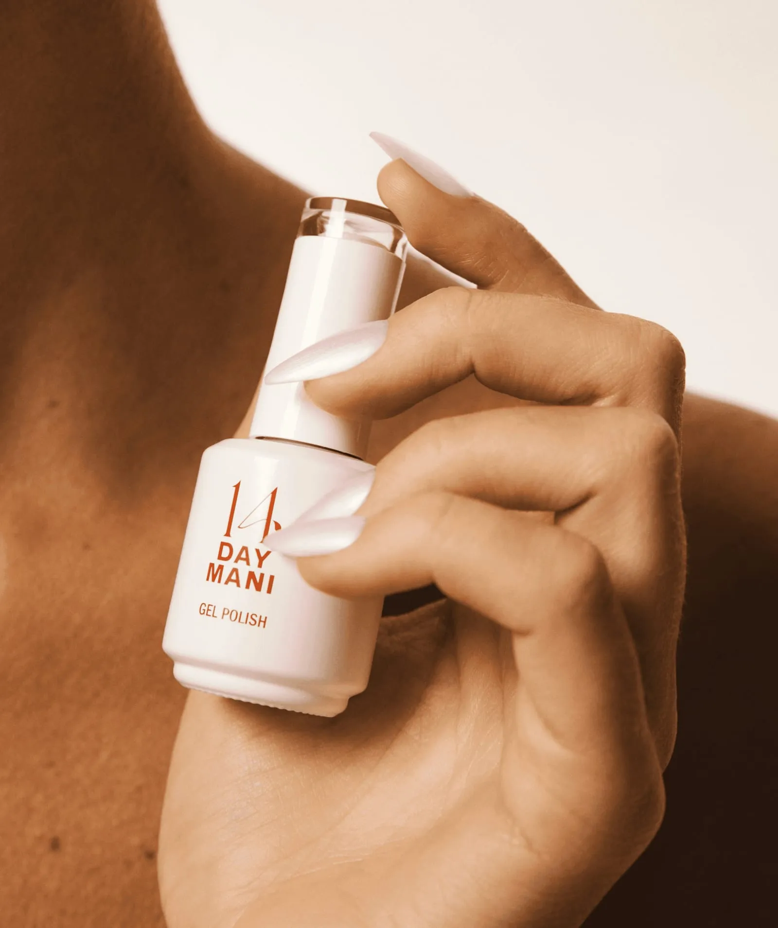 Hand with pale pink almond nails holding a 14 Day Mani gel polish bottle from the HEMA-free collection