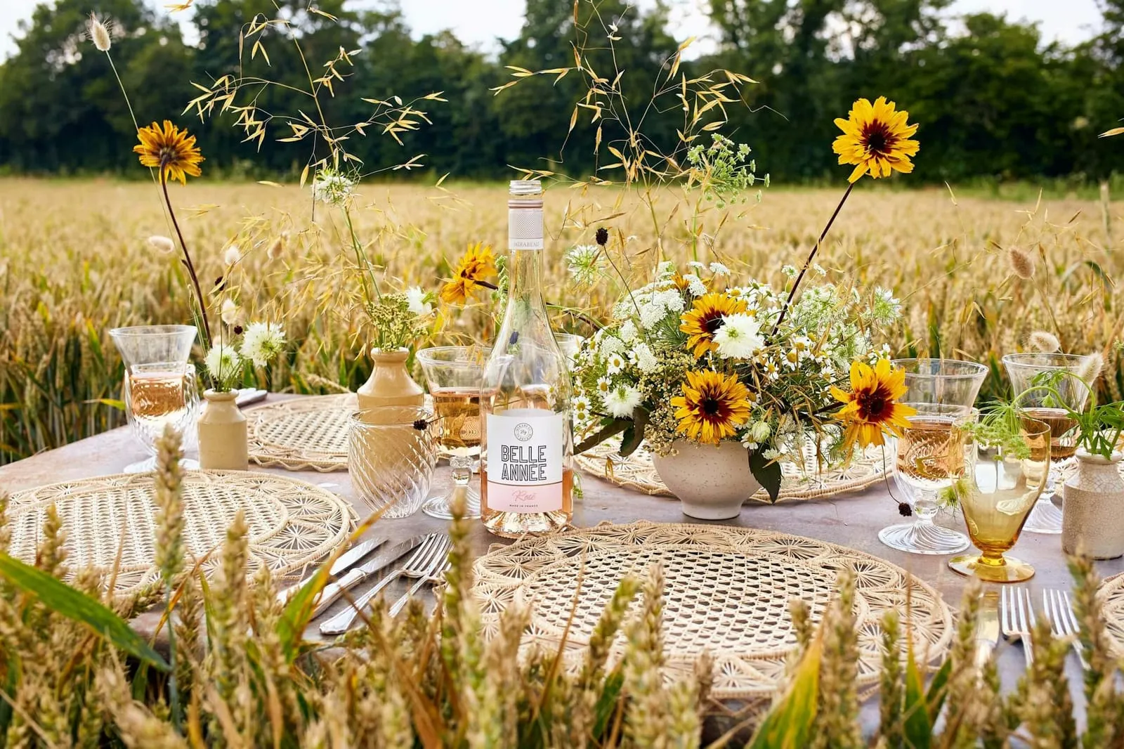 Rose wine and a sunflower centrepiece on a wheat-field table set with woven placemats and glassware