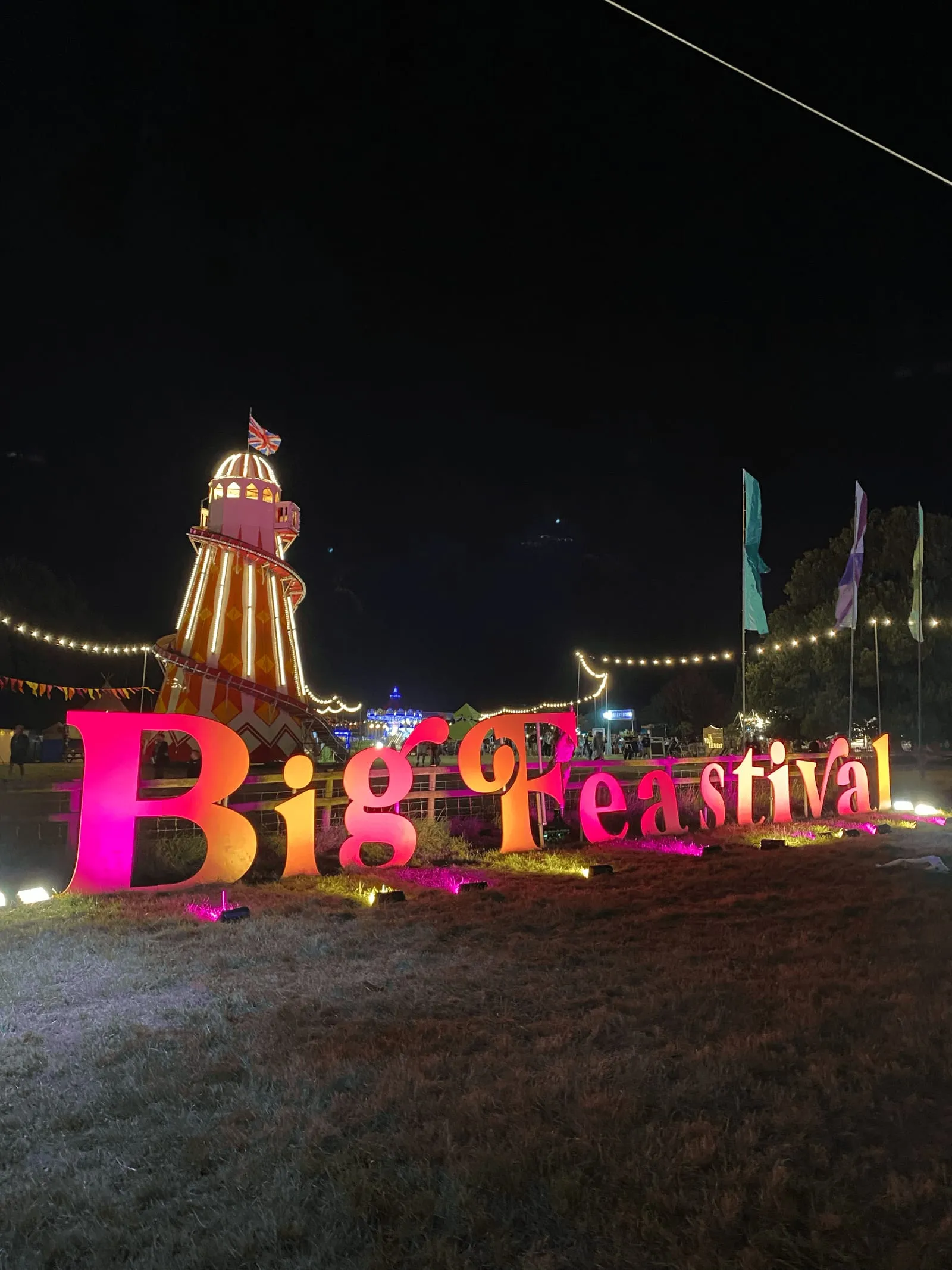 The Big Feastival sign and helter skelter lit up in pink and orange at night