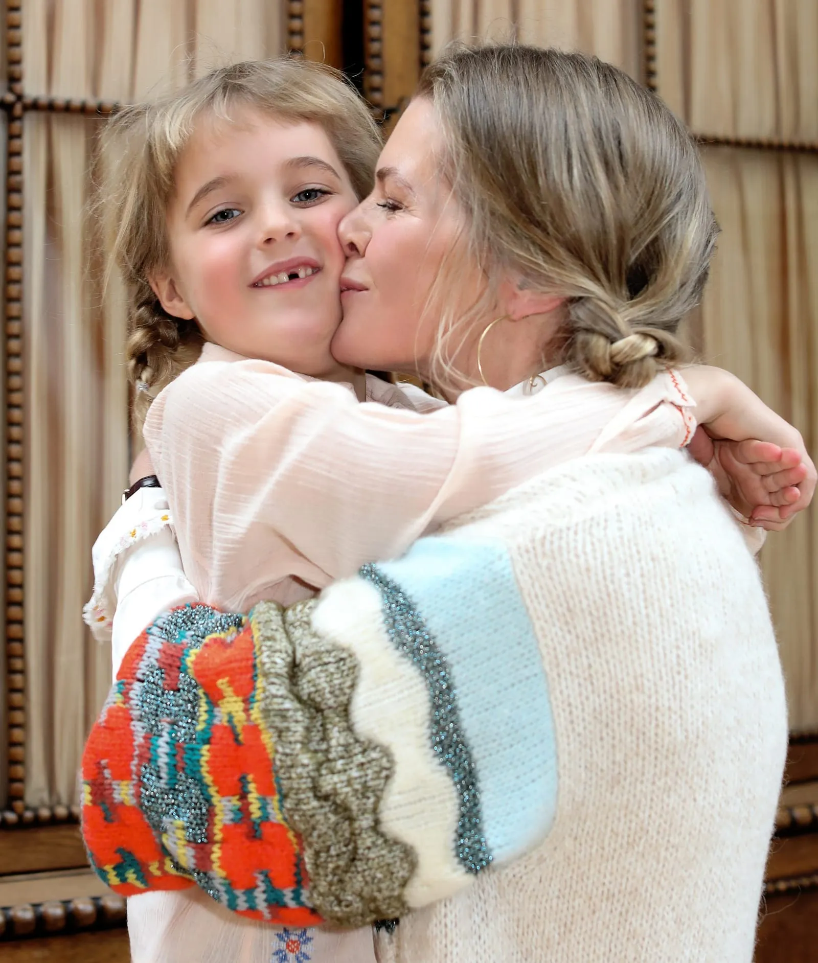 Mother kissing her young daughter on the cheek, both wearing plaits