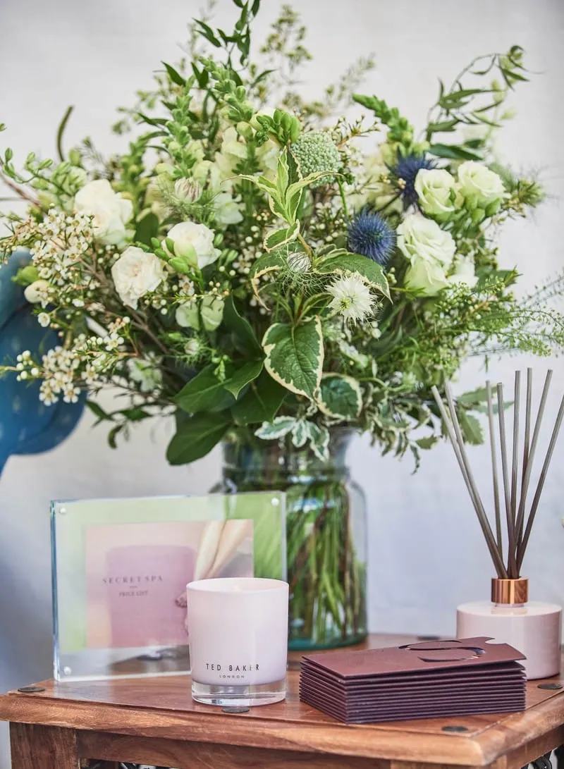 Spa reception table with a white and green flower arrangement, candle, reed diffuser and Secret Spa price list