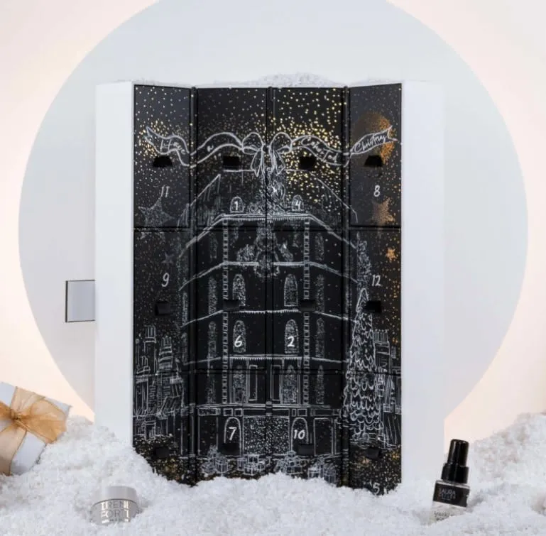 Black beauty advent calendar with numbered drawers and a white line-drawn townhouse, set in fake snow
