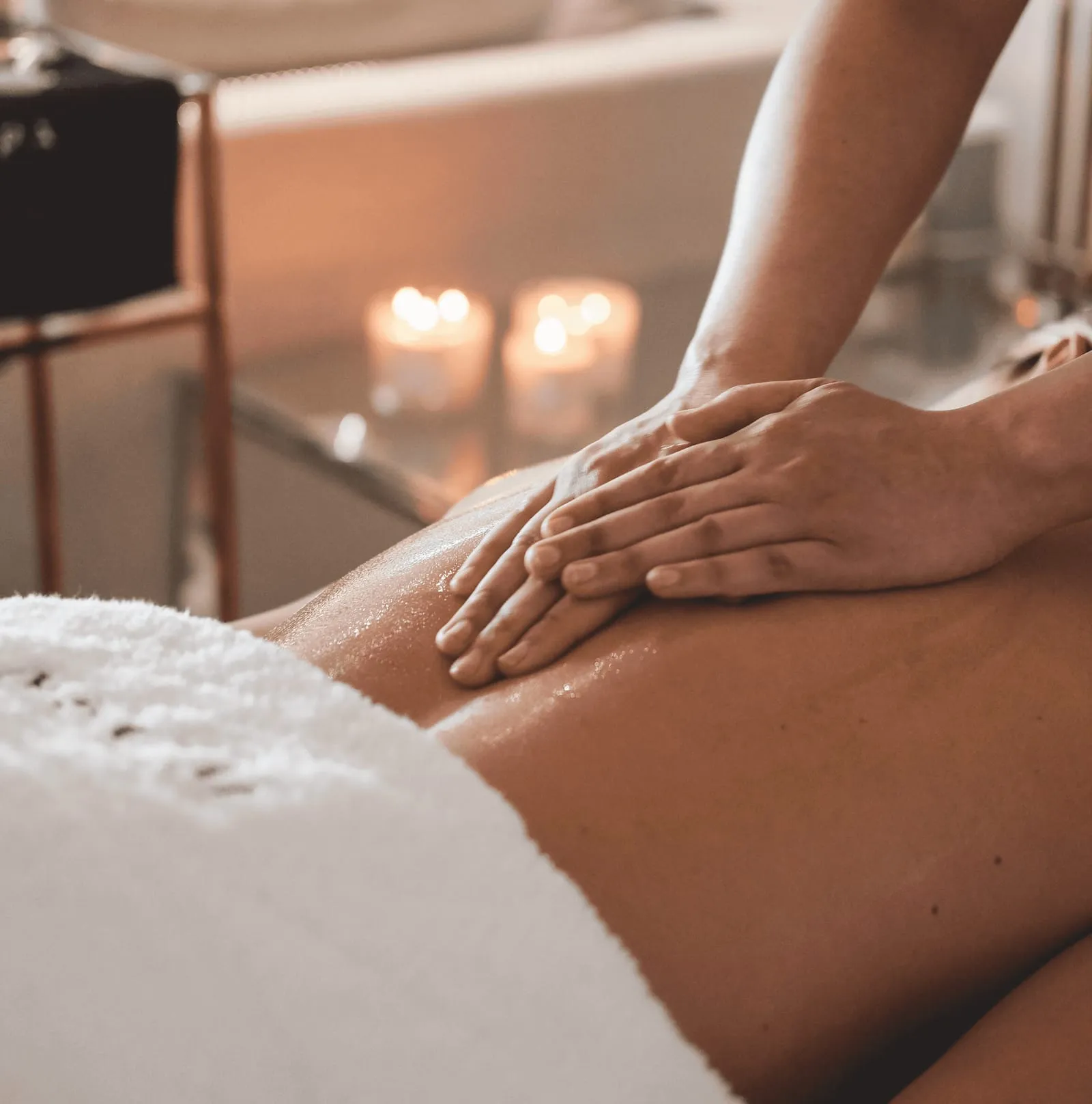 Therapist's hands working oil into a guest's back on a massage bed by candlelight