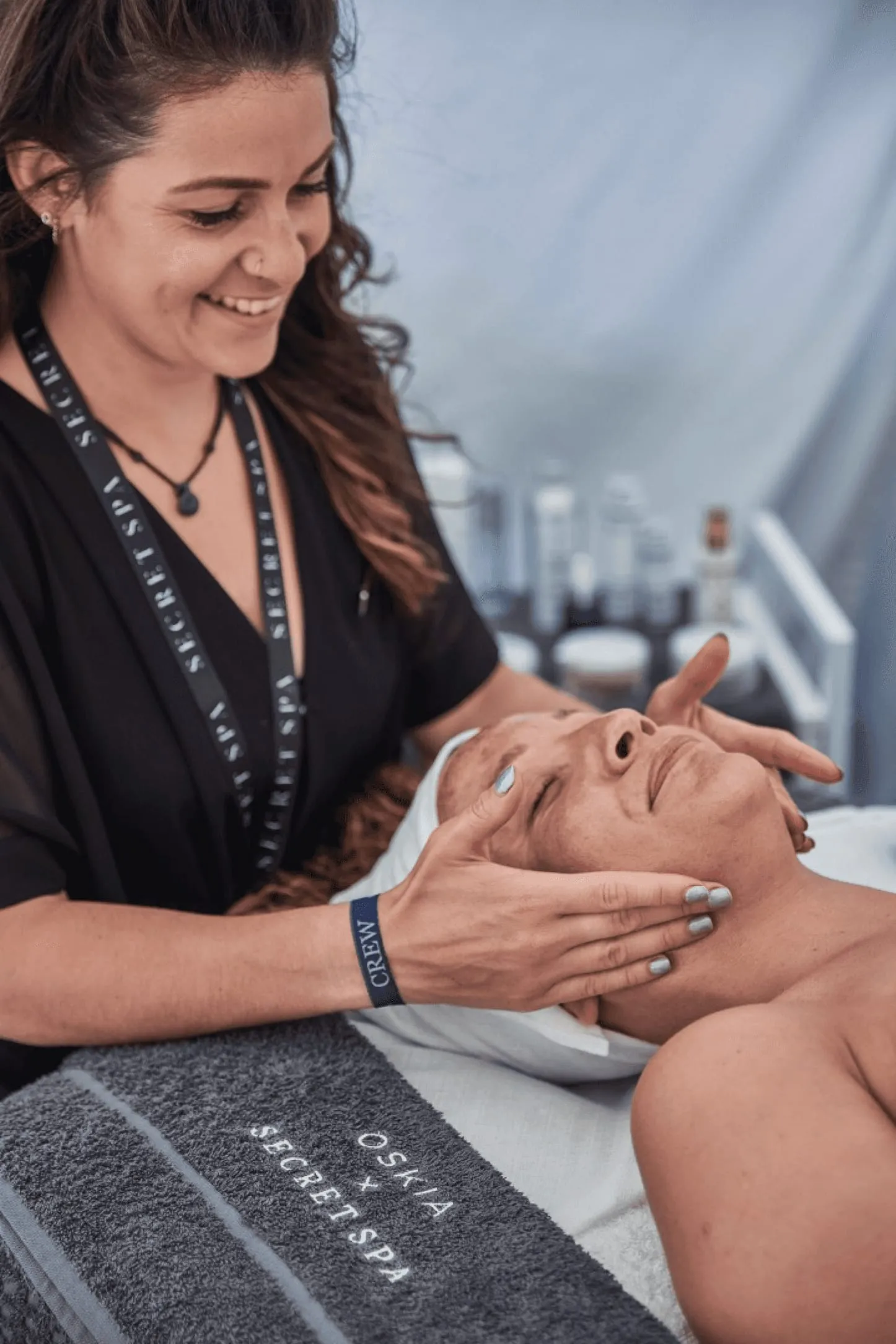 Secret Spa therapist giving a facial massage on a treatment bed with an OSKIA x Secret Spa towel
