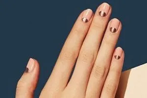 Manicure with nude polish and metallic rose gold half-moon detail against a navy background