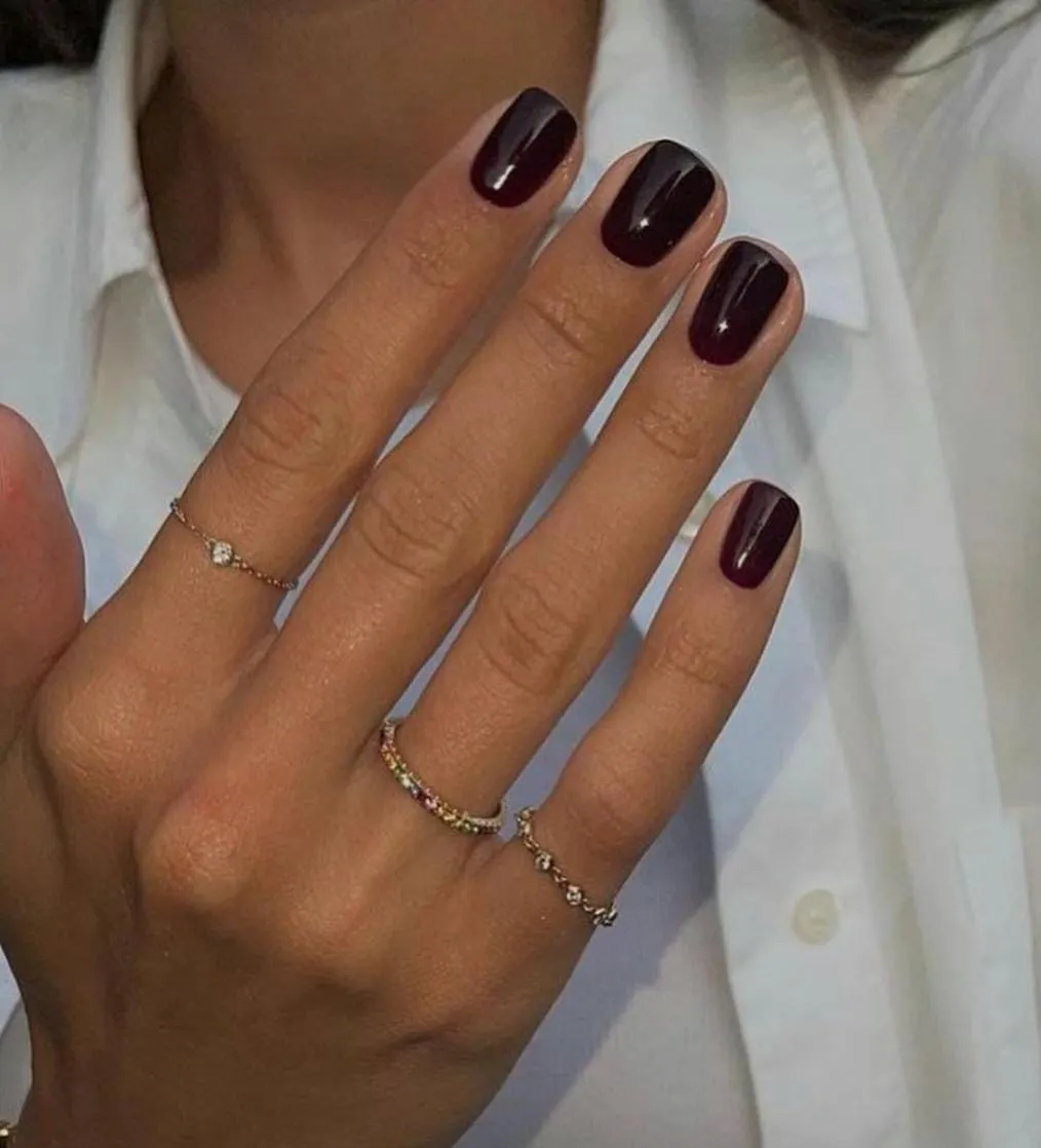 Short square nails painted in a glossy deep burgundy, held against a white shirt