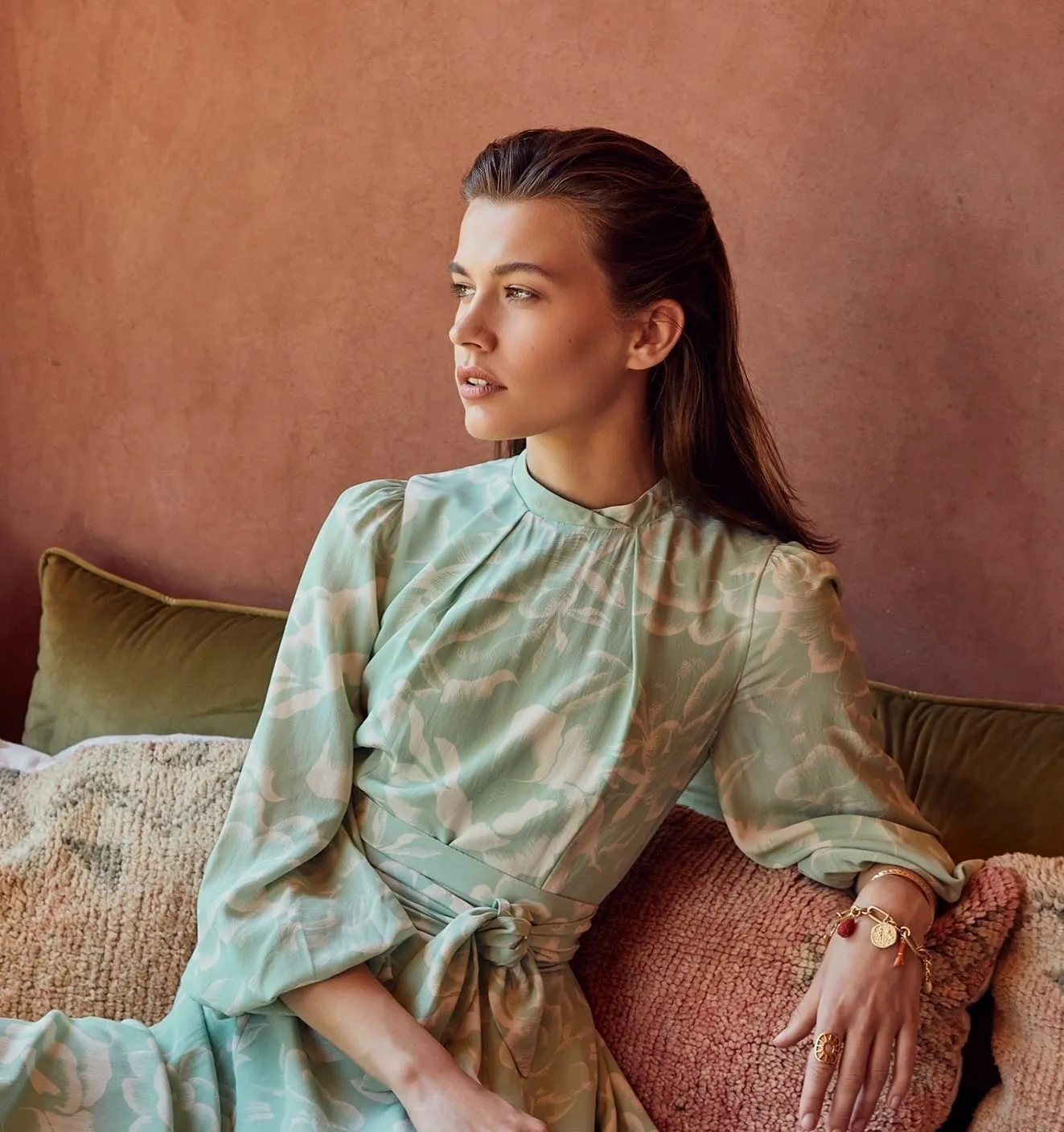 Model in a mint floral dress with a sleek half-up style and soft natural make-up against a terracotta wall