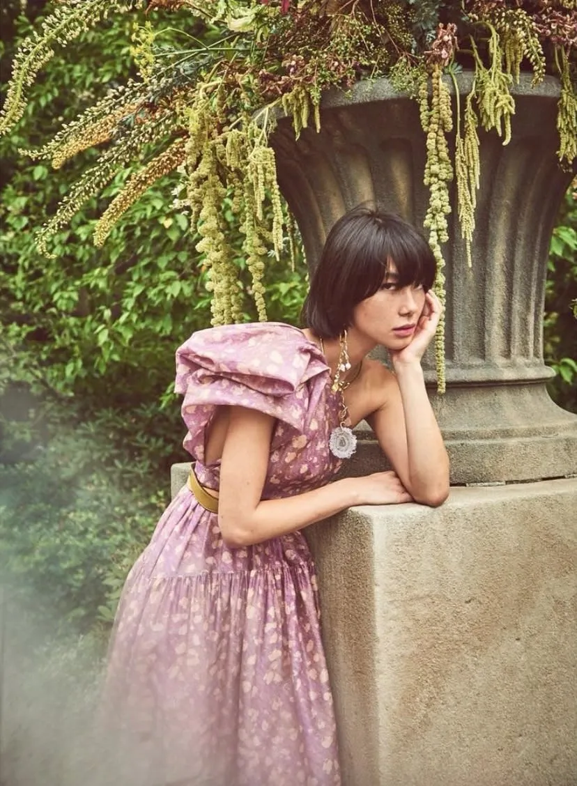 Short textured bob with a full fringe, worn with a lilac floral dress in a garden
