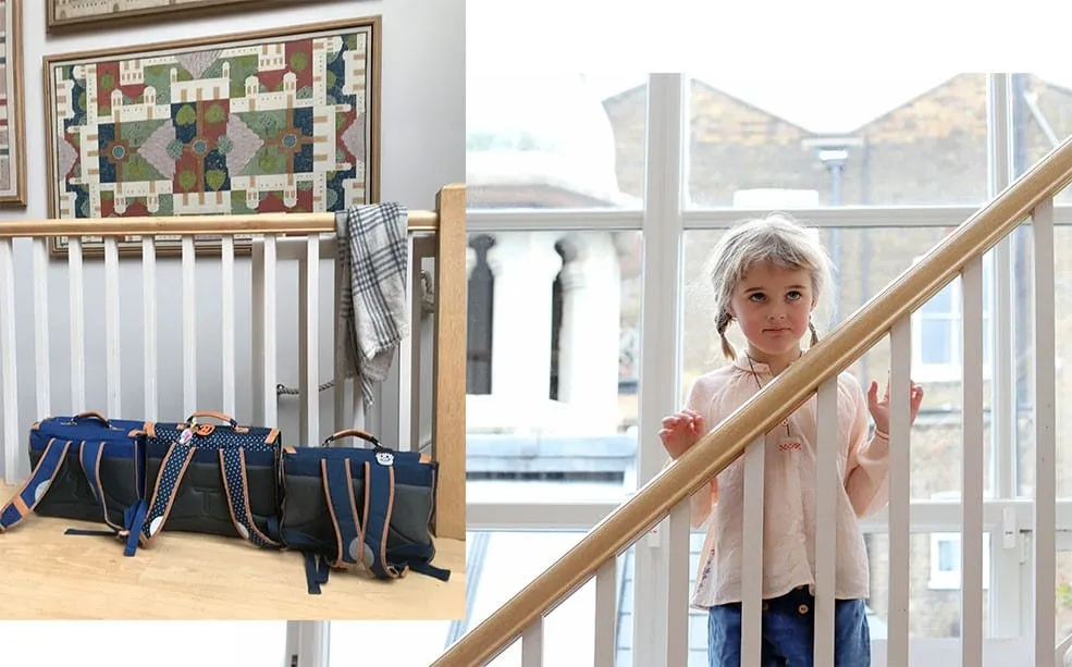 Navy school satchels lined up on a landing, and a young girl with plaits standing on the stairs