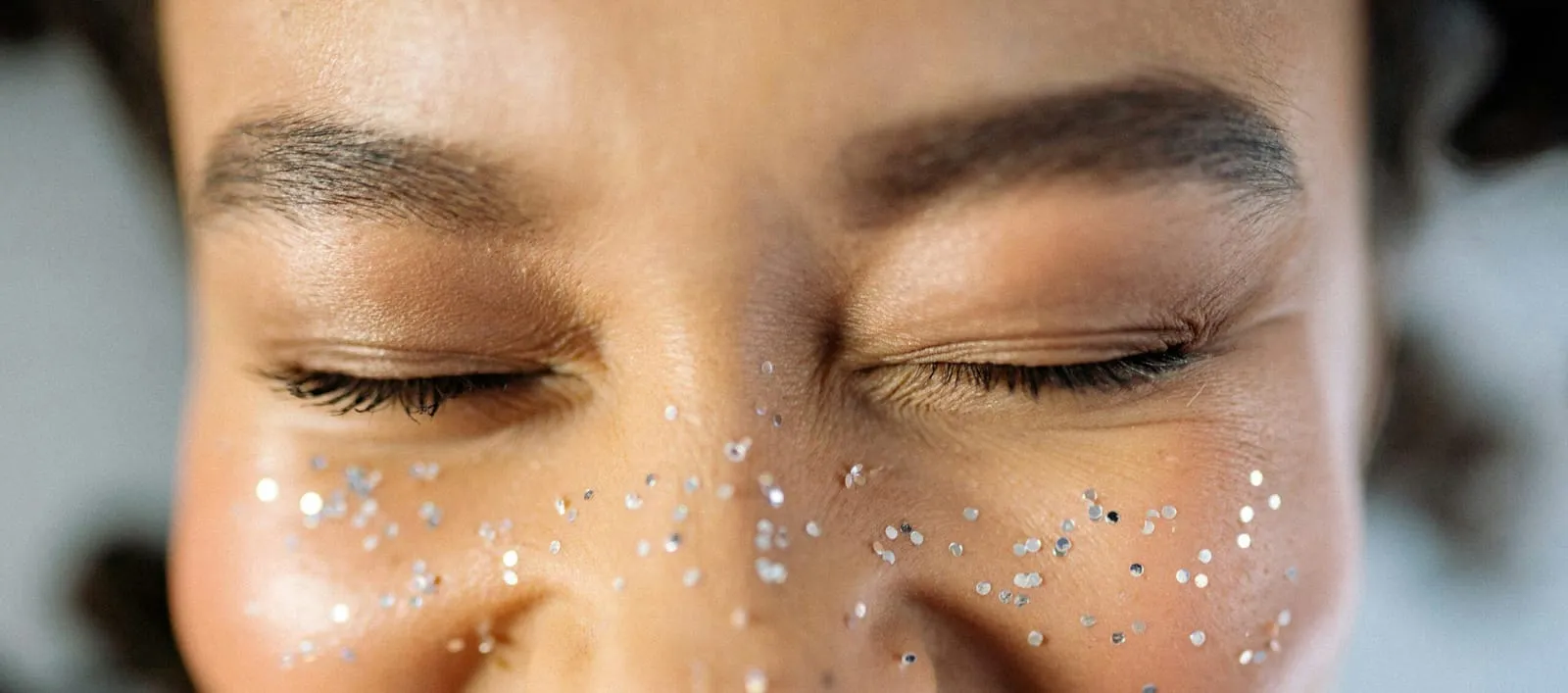 Close-up of closed eyes with silver glitter scattered across the cheeks like freckles