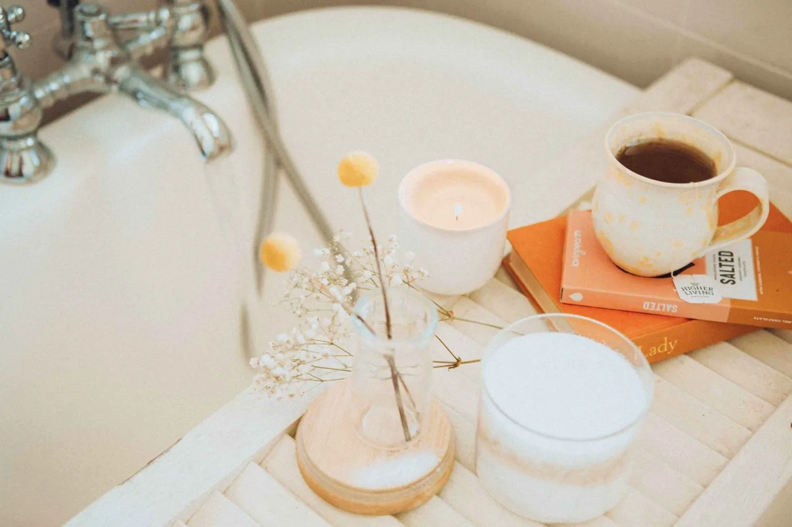 Bath tray across a roll-top tub holding a lit candle, dried flowers, tea and a bath salt jar