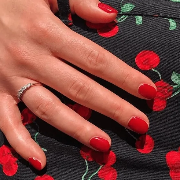 Short oval nails in classic glossy red, resting on a black cherry-print dress