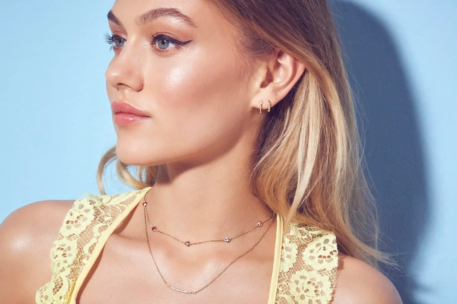 Side profile with glowing highlighter, winged black liner and a fine gold chain necklace
