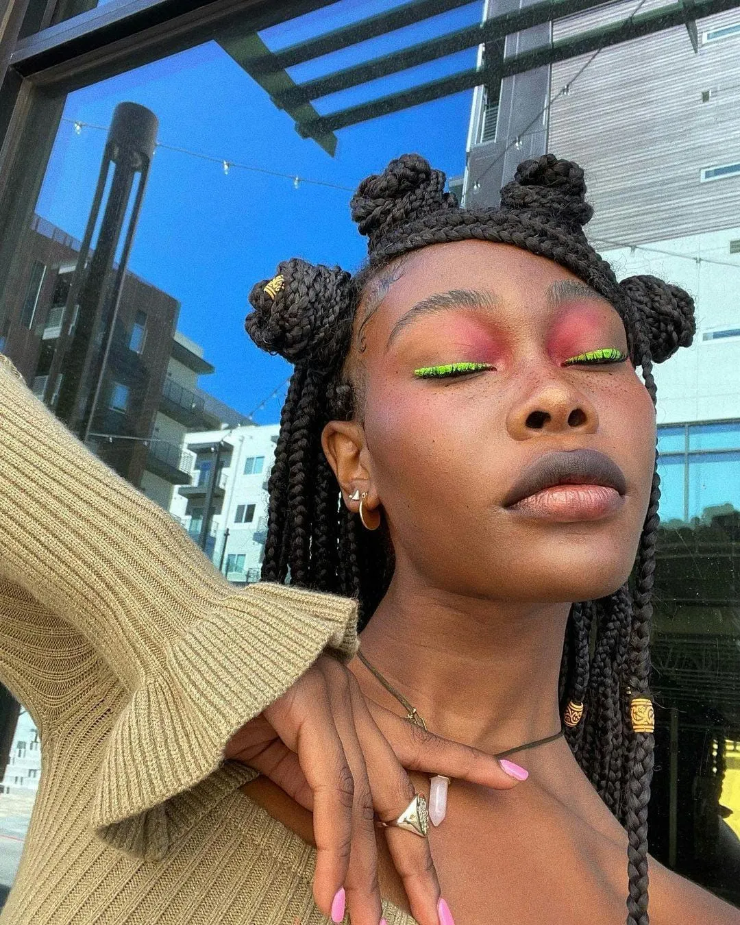 Neon green graphic eyeliner over coral pink lids, hair styled in braided space buns