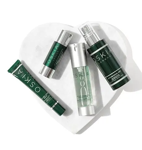 Four OSKIA skincare bottles and a tube arranged on a white marble heart-shaped dish
