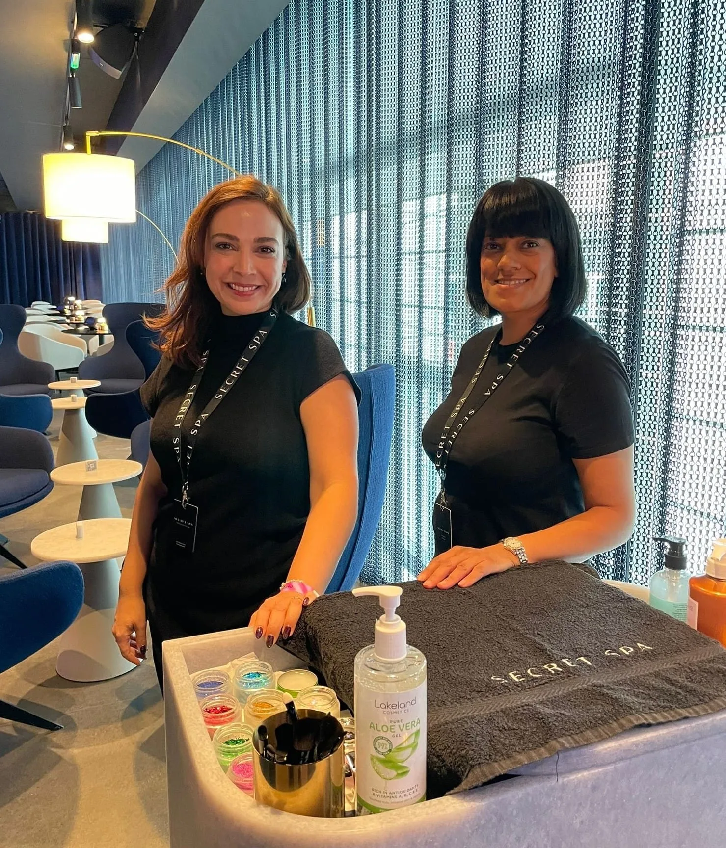 Two Secret Spa therapists at a nail station with glitter pots and a branded towel in the Sky VIP lounge