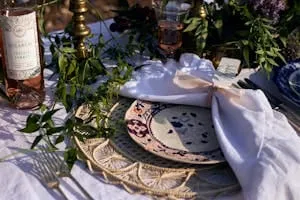 Tablescape place setting with a patterned plate, white knotted napkin and woven raffia charger