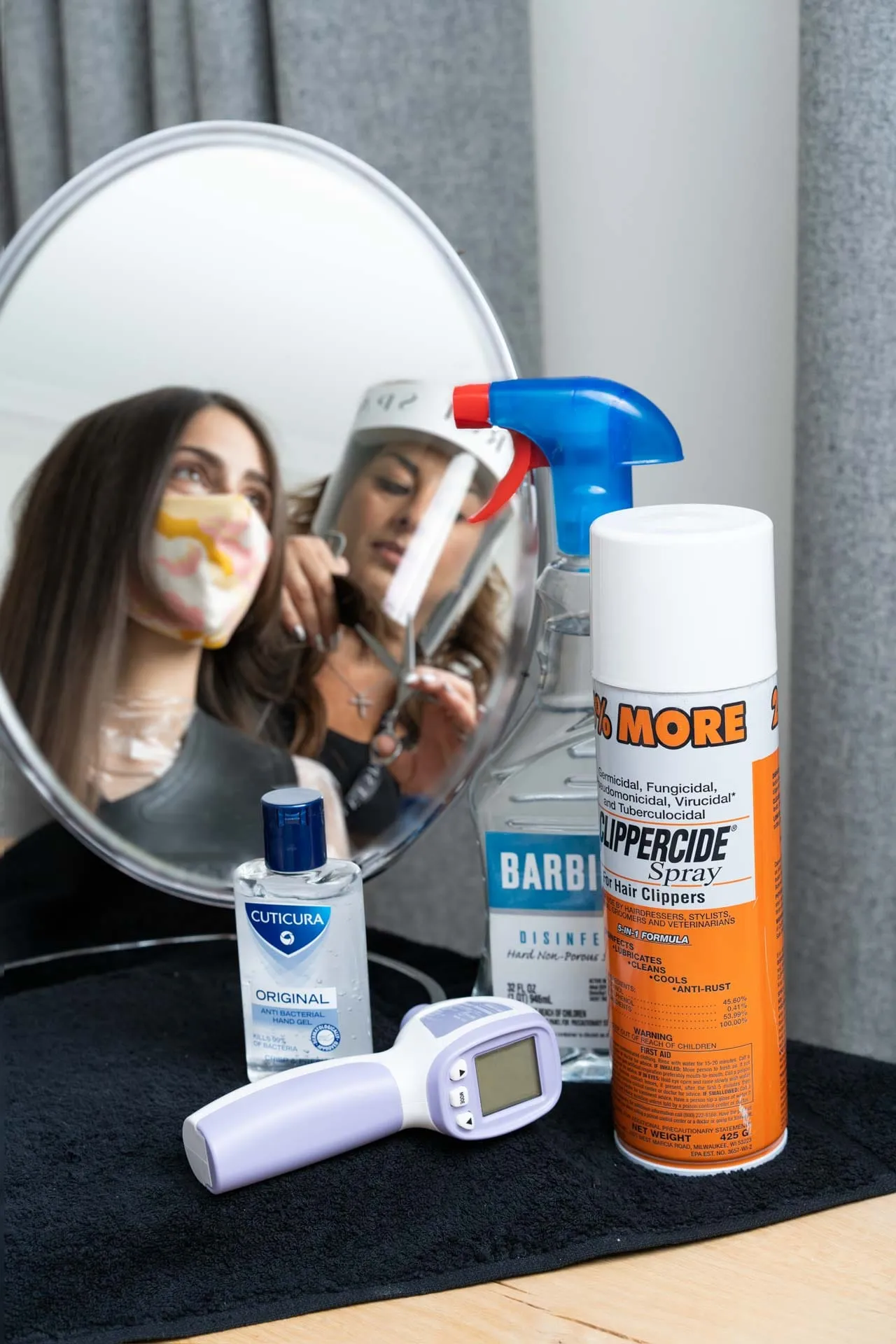Home haircut hygiene kit: hand gel, disinfectant spray, Clippercide and a thermometer by a mirror