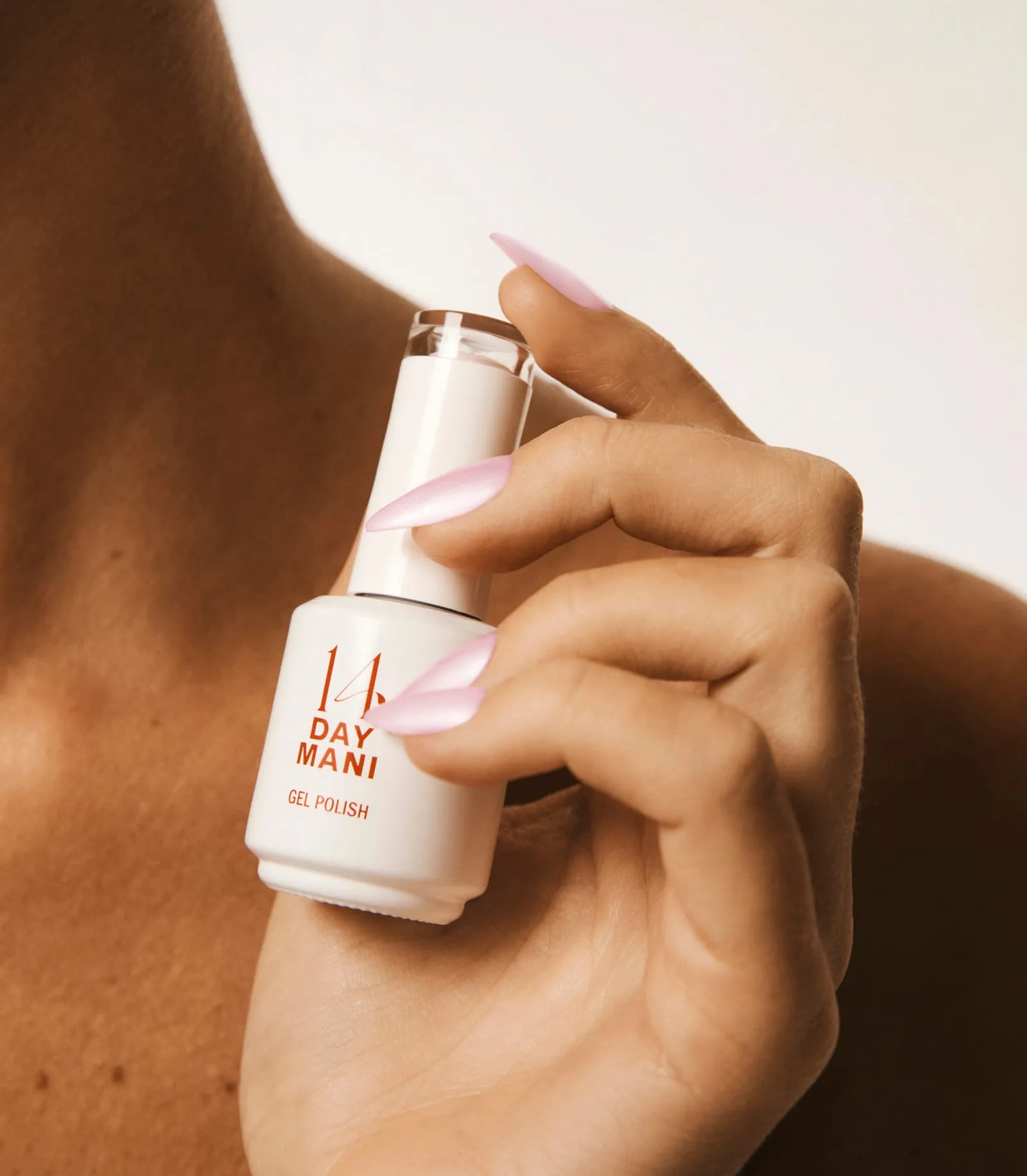Hand with long pale pink almond nails holding a 14 Day Mani gel polish bottle