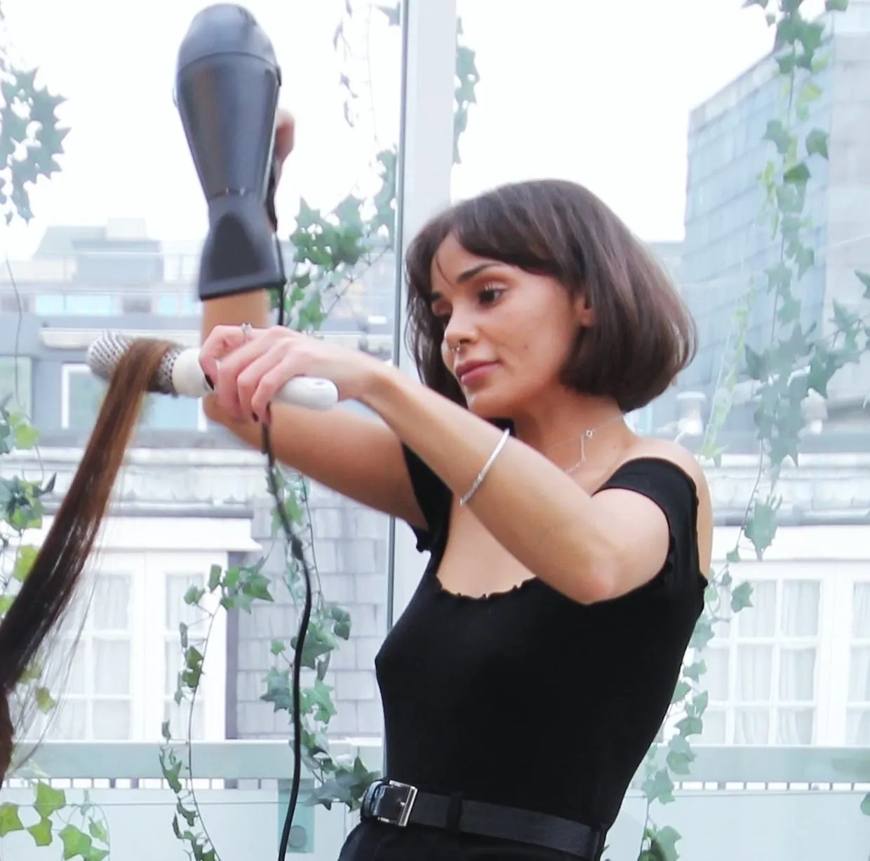 Secret Spa Stylist blow drying long hair with a round brush beside a window