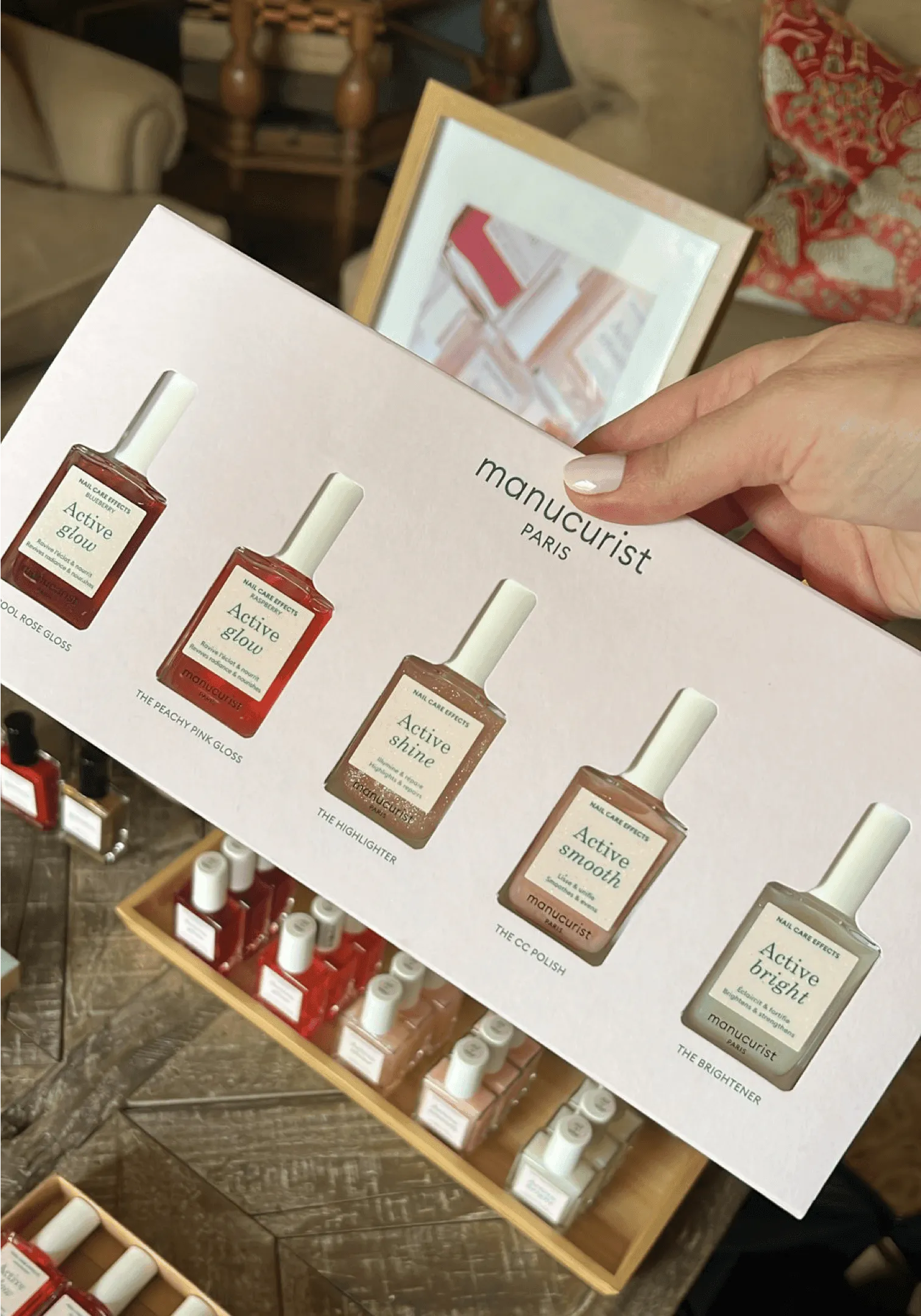 Hand holding a Manucurist Paris Active Glow shade card above a tray of nail polish bottles