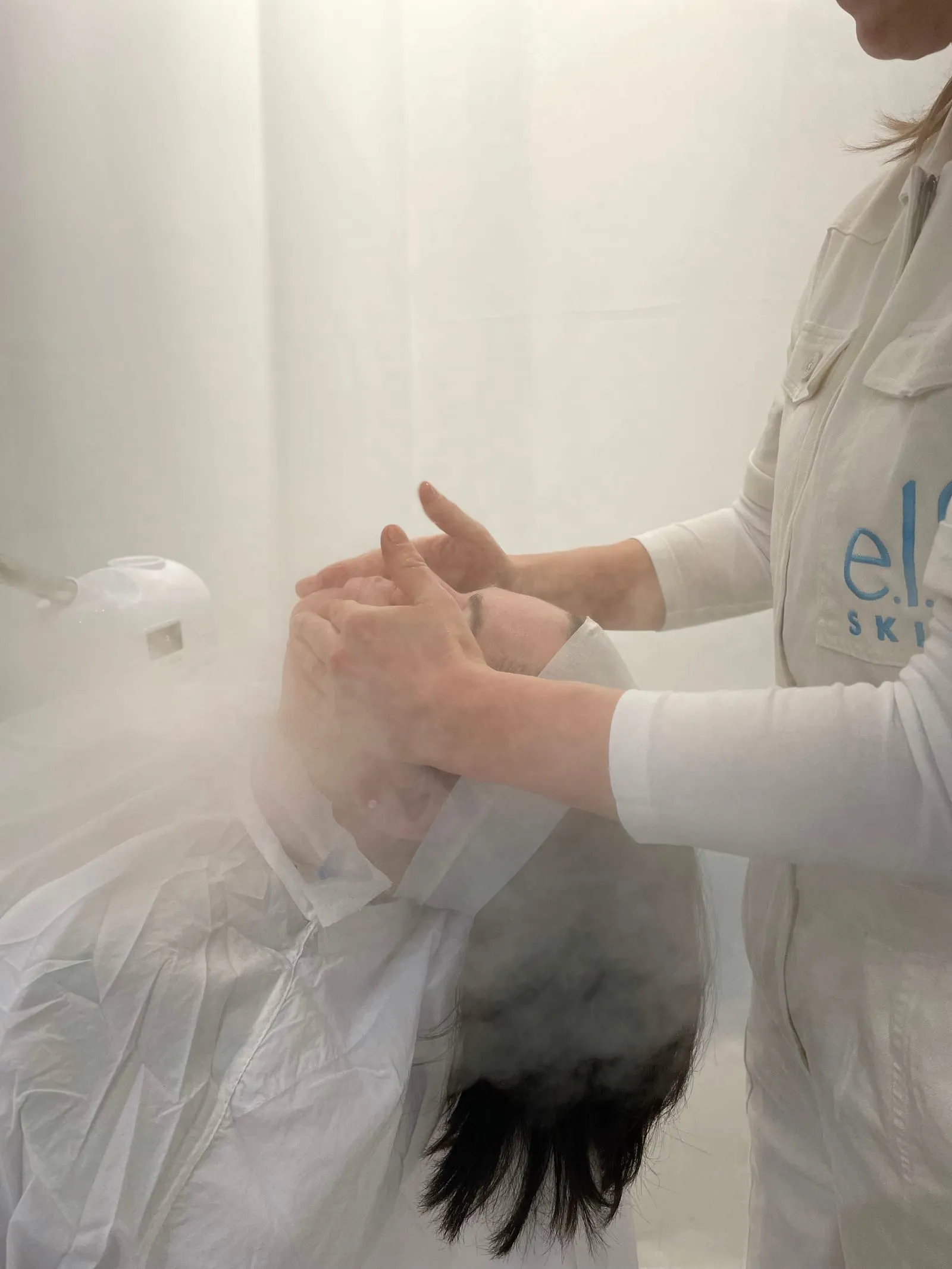 e.l.f. SKIN specialist performing a facial in a steam-filled white treatment room