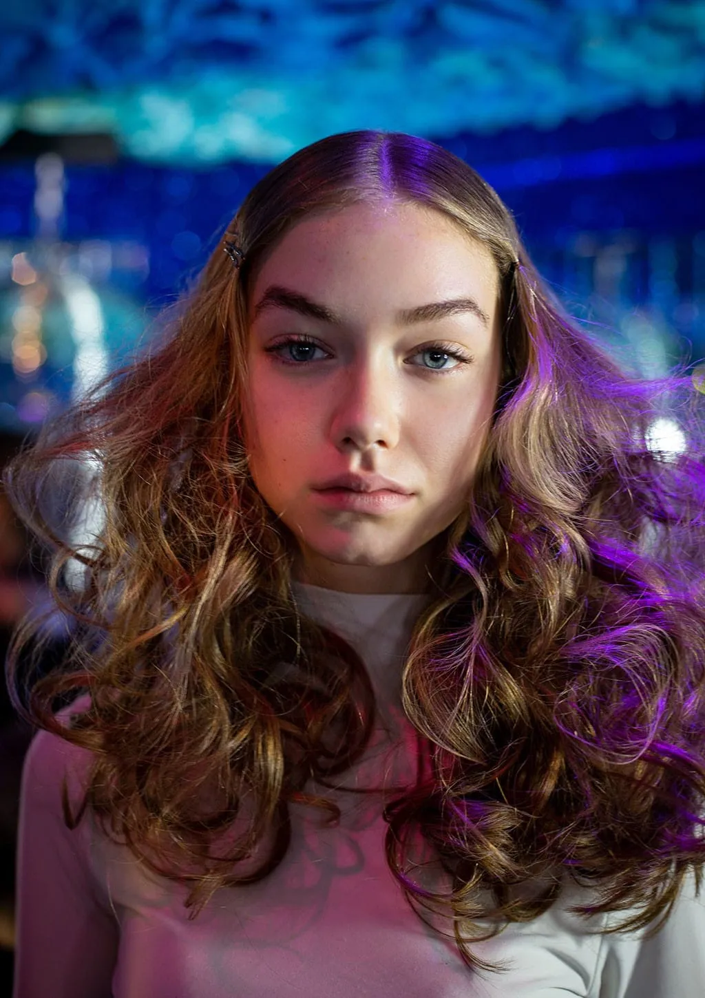 Voluminous curly blow-dry with a centre parting, lit by blue and purple disco lighting