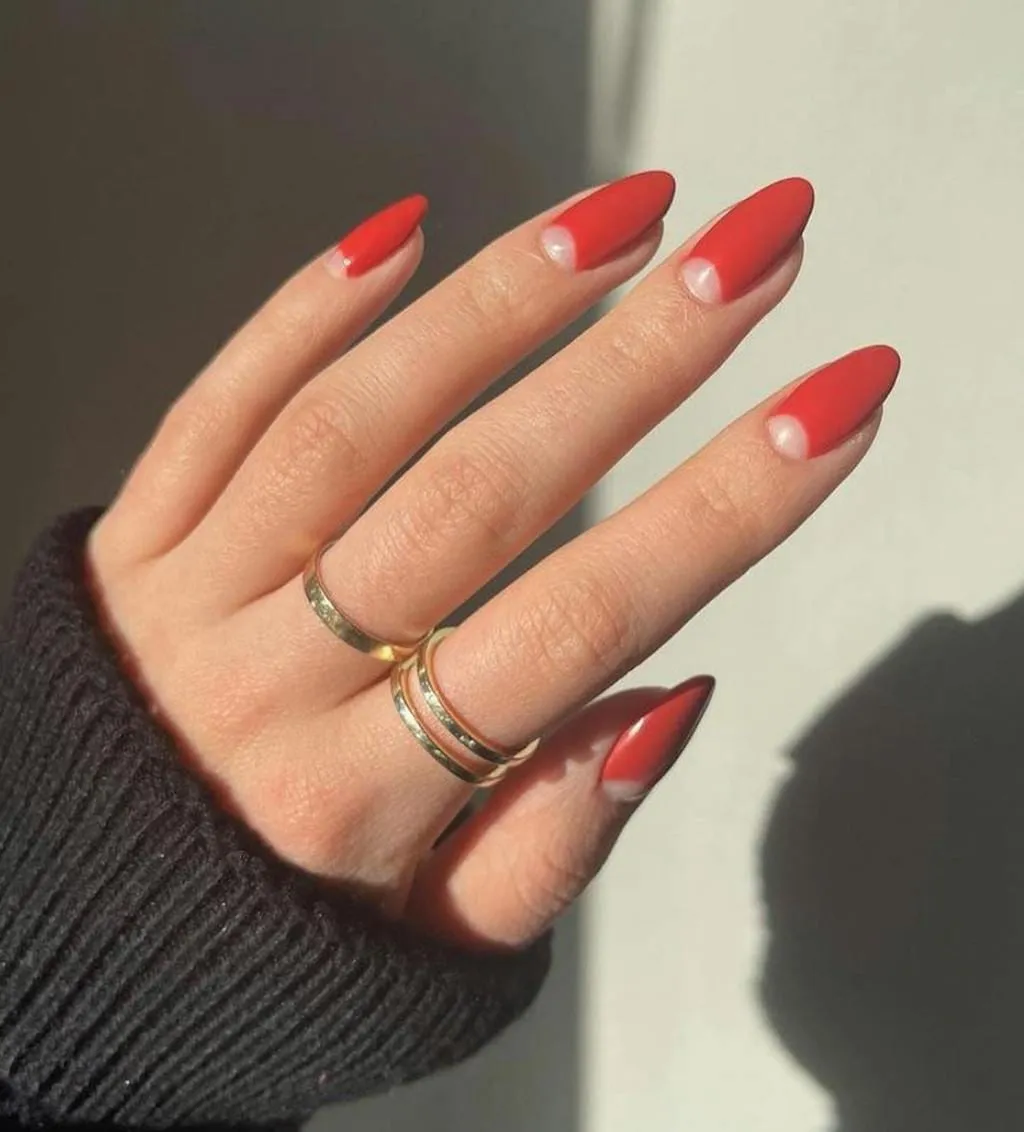 Reverse manicure on almond nails, red polish left bare in a half-moon at the cuticle