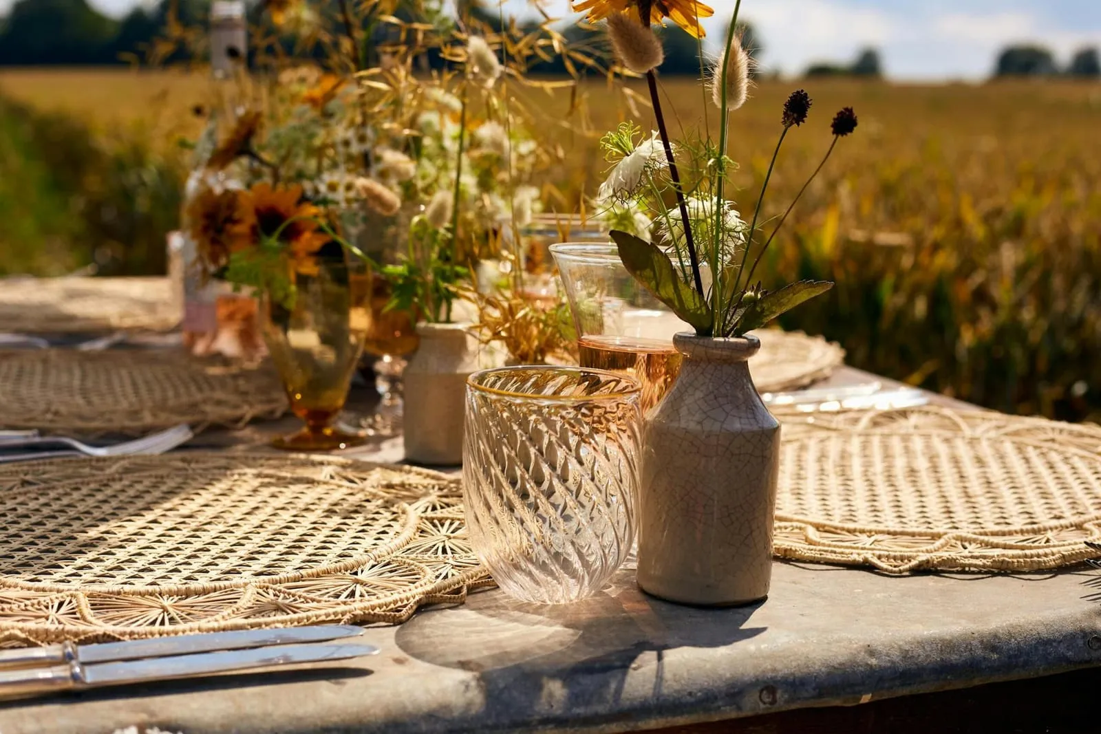 Woven placemats, cut glass tumblers and wildflowers in stoneware vases on a rustic outdoor table
