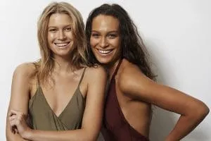 Two people with even golden spray tans smiling side by side in camisole tops