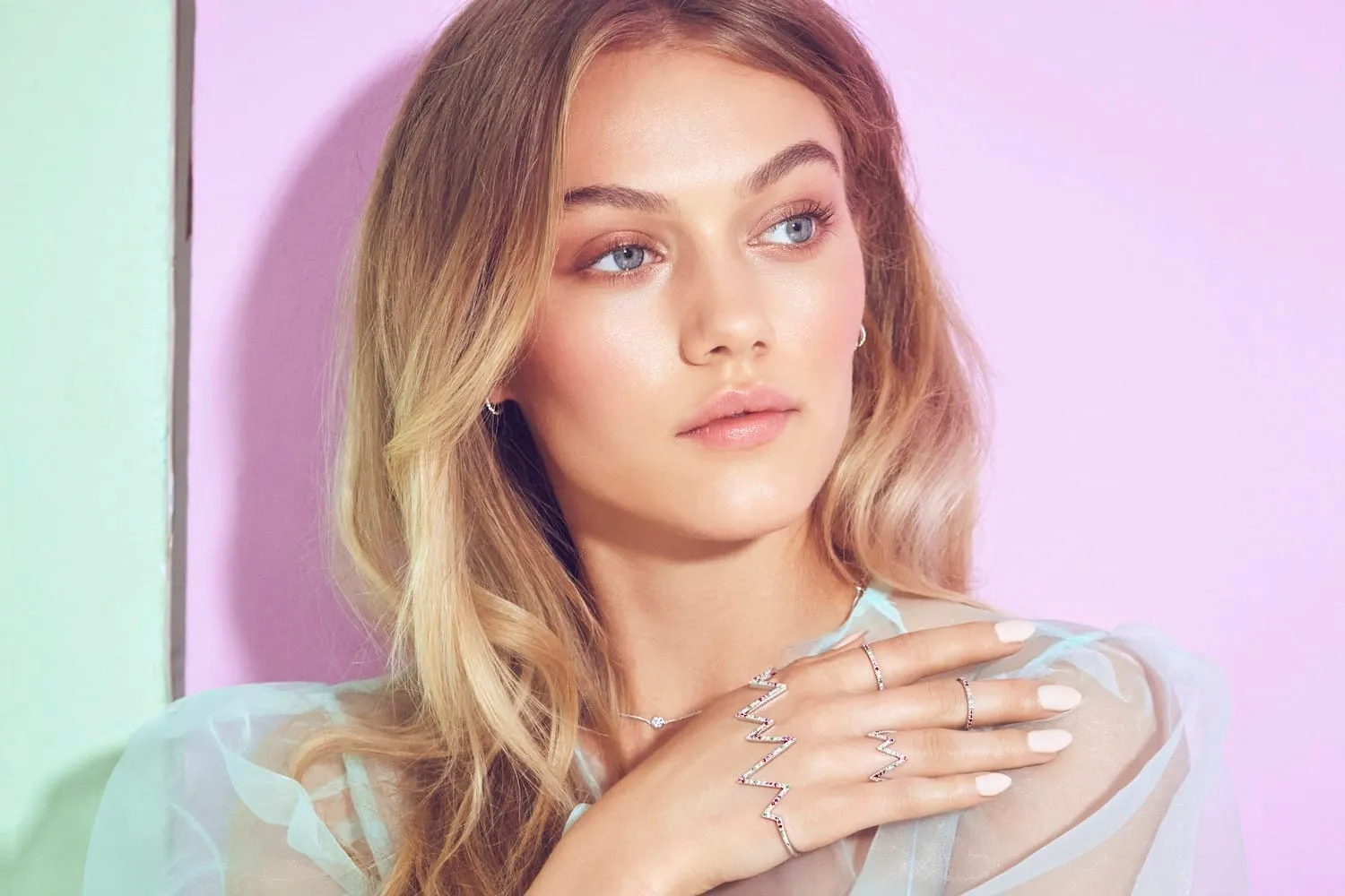 Fresh dewy make-up and pale nude nails, hand wearing zigzag gem rings resting on the shoulder