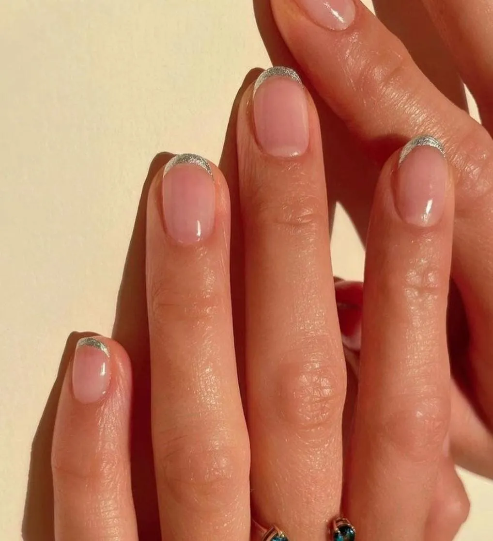 Short round nails with fine silver glitter French tips over a sheer pink base