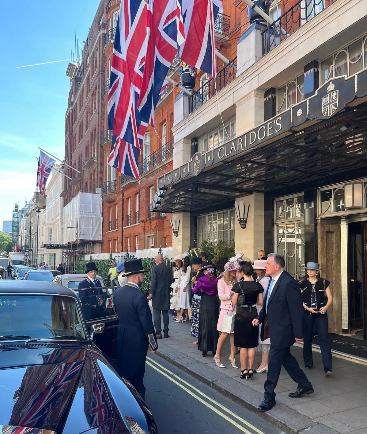Guests in hats arriving at Claridge's in Mayfair with Union Jack flags overhead