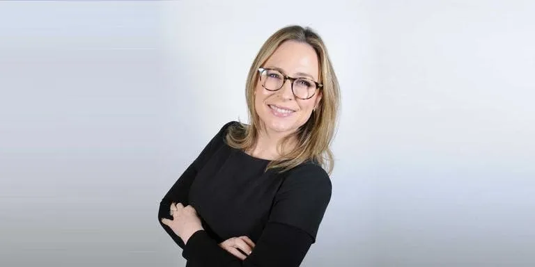 Portrait of Secret Spa co-founder Emily, arms folded, in a black top and glasses