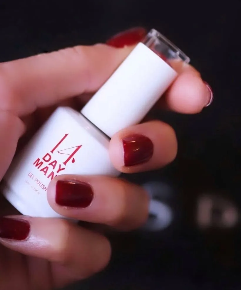 Hand with deep red gel nails holding a 14 Day Mani gel polish bottle