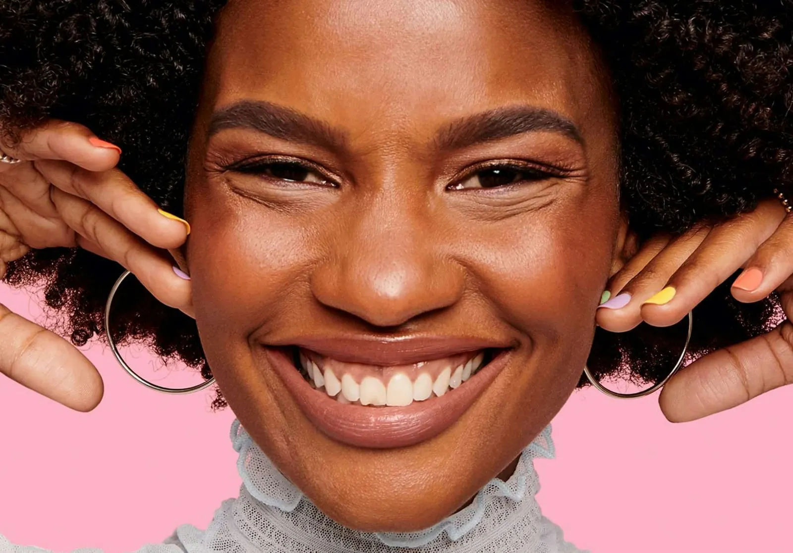 Close-up of a smiling face with softly brushed-up, feathered brows and a pastel manicure