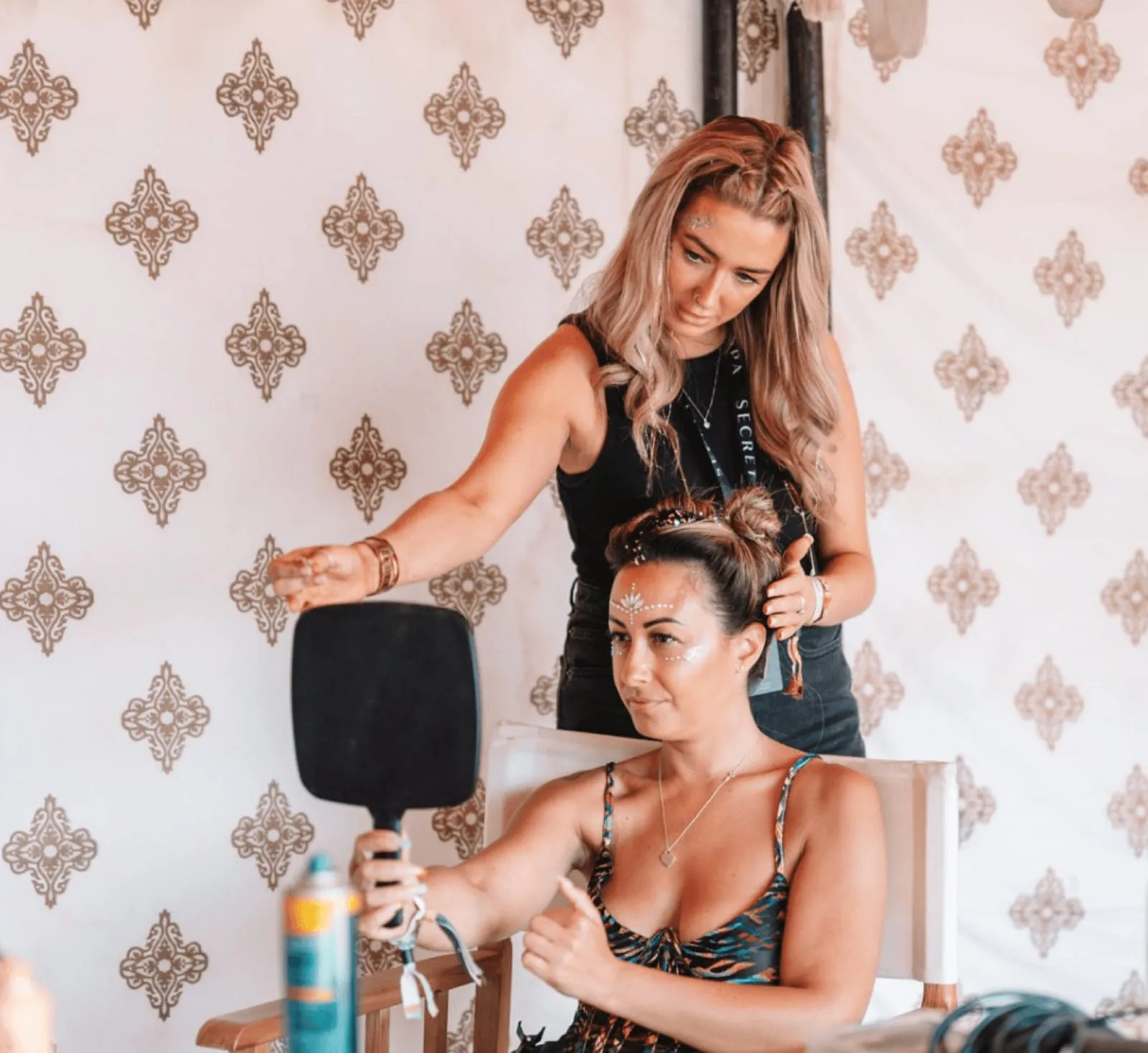 Secret Spa Stylist finishing a festival updo with glitter and face gems inside a decorated tent