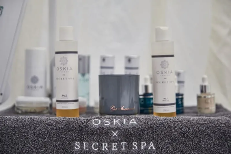 OSKIA x Secret Spa treatment products lined up on a branded grey towel