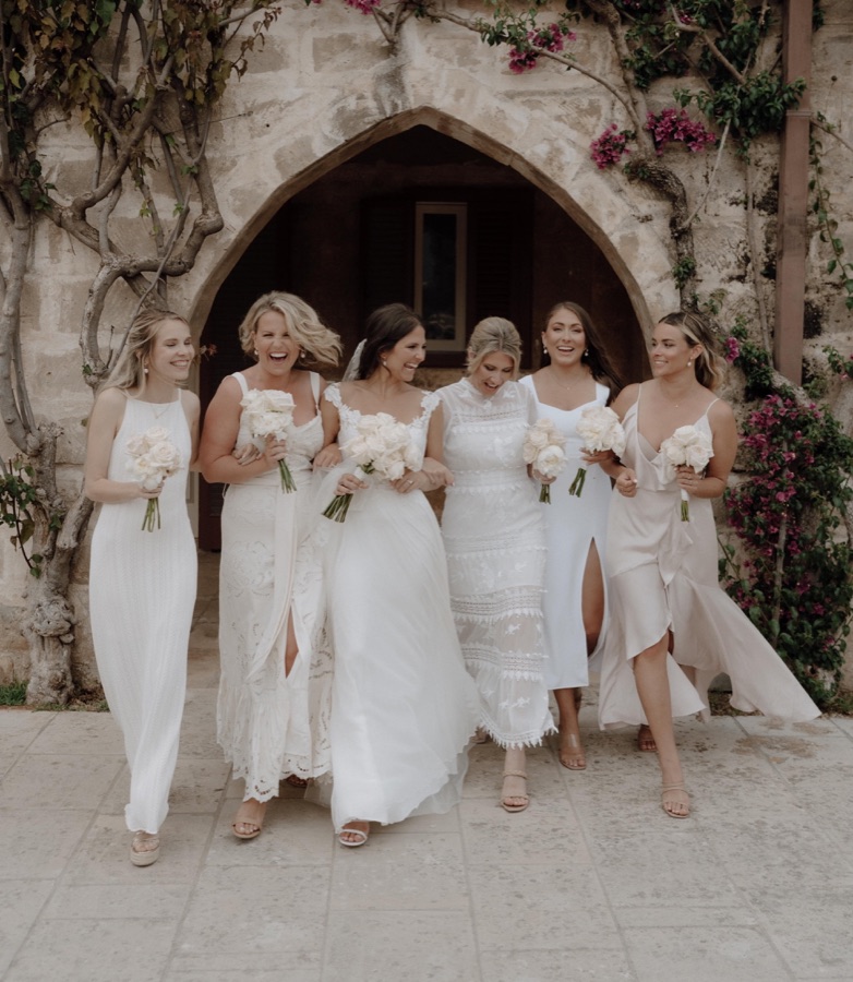 Bride and five bridesmaids walking arm in arm in ivory, every one of them in loose bridal waves
