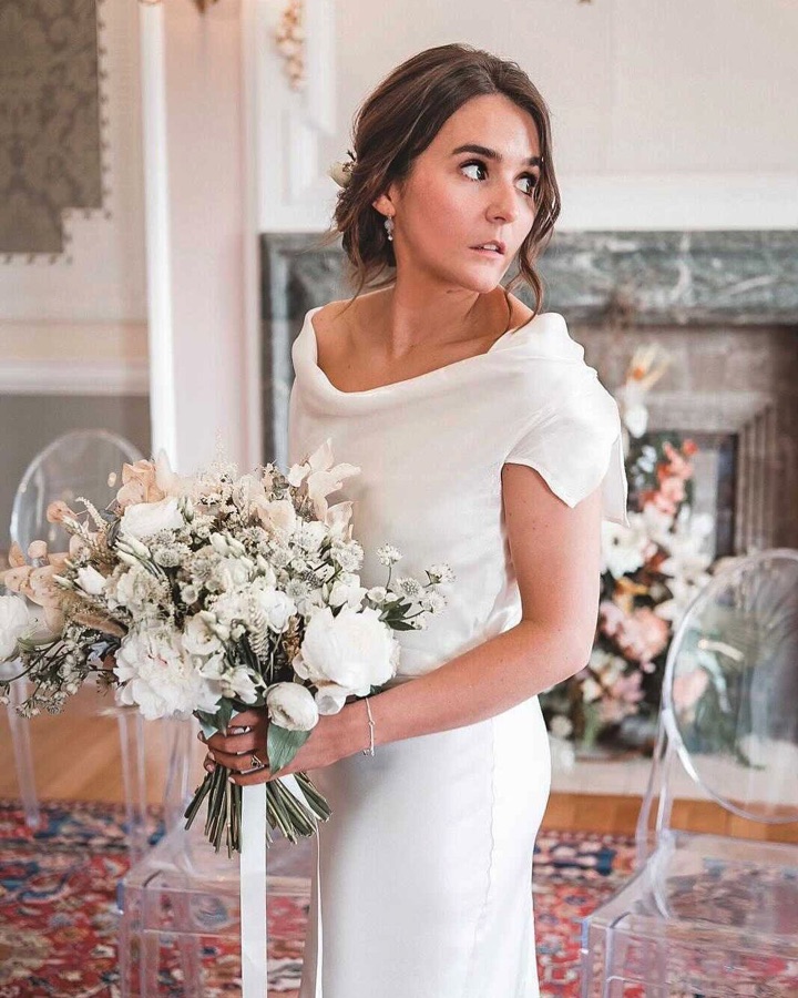 Bride holding a white bouquet, hair in a soft low chignon with dewy bridal make-up
