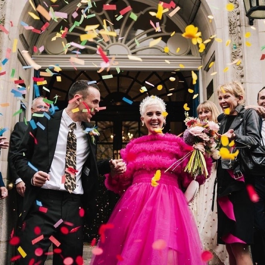 Bride in a pink tulle dress leaving a London register office under confetti, hair in a cropped platinum style