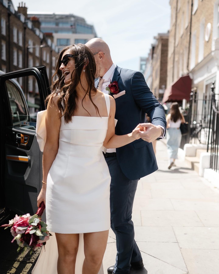 Bride stepping out of a black cab in a short dress, hair in tousled waves